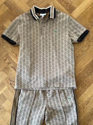 Beige set från Lacoste med mönster - Snygg tracksuit från Lacoste, en pique med långa byxor perfekt till sommaren. Köpt för 3000kr i Lacoste butik. Pris kan diskuteras vid snabb affär :)