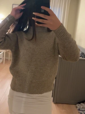 Beige stickad tröja - Mysig beige stickad tröja med hög krage och långa ärmar. Tröjan har en rak passform och ribbstickade muddar vid ärmslut och nederkant. Perfekt för kyliga dagar och enkel att matcha med olika outfits.
