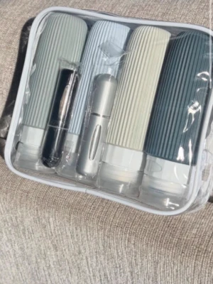 Resekit med flaskor och tvättpåse - Praktiskt resekit med fyra mjuka silikonflaskor i olika färger (grå, blå, beige, mörkgrå) och två små parfymflaskor i svart och silver. Allt kommer i en genomskinlig necessär med vit kant och medföljande tvättpåse. Perfekt för att ta med schampo, balsam och parfym på resan.