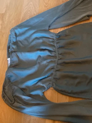 Grön långärmad blus med resår - Stilren grön blus med lång ärm och resår i midjan som ger en snygg siluett. Blusen har en enkel, rund halsringning och är tillverkad i ett mjukt, lätt tyg som faller fint. Perfekt för dig som gillar en avslappnad men ändå chic look.