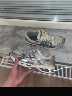 Silvriga Asics sneakers med mesh - Säljer ett par riktigt snygga Asics sneakers i silver och vitt med svarta detaljer. Skorna har en sportig vibe med mesh-ovandel för bra andningsförmåga och reflekterande partier. Klassisk låg modell med bekväm sula och tydliga Asics-loggor på sidorna.