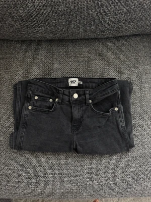 Svarta bootcut med knappar - Säljer ett par svarta bootcut jeans från Lager 157 med klassisk femficksdesign och silverfärgade nitar. Jeansen har låg midja med full length. 