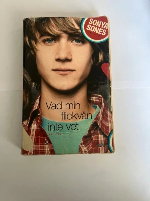 Vad min flickvän inte vet - Ungdomsroman med färgstarkt omslag i rött, svart och turkost. Boken handlar om relationer och kärlek på gymnasiet och är skriven av Sonya Sones. Mjukt omslag i papper, del två i en serie. Perfekt för dig som gillar romantik och drama.