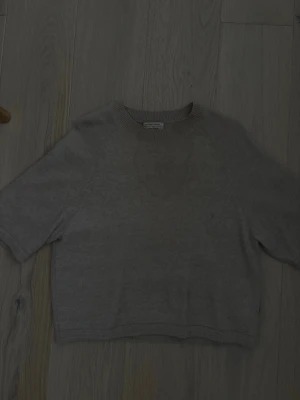 Beige kortärmad tröja & Other Stories - Kortärmad beige tröja från & Other Stories Stockholm Atelier. Tröjan har rund halsringning med ribbad kant och är gjord i mjukt material. Enkel och stilren design som passar perfekt till jeans eller kjol. Har en fläck men går säkert bort