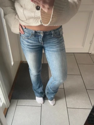 Ljusblå bootcut jeans med låg midja - Säljer ett par ljusblå bootcut jeans med låg midja och klassisk femficksdesign. Jeansen har snygga slitningar och tvättade detaljer framtill och baktill. Perfekta till en avslappnad och trendig look.