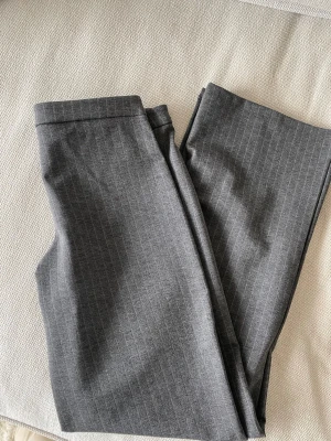 Grå kostymbyxor med diskreta ränder - Snygga grå kostymbyxor med tunna, diskreta kritstrecksrandiga linjer. Klassisk rak passform och bälteshällor i midjan. Perfekta för en stilren look. Materialet känns mjukt och har en lätt stretch för extra komfort. Upplevs lågmidjade. Aldrig använda med prislapp