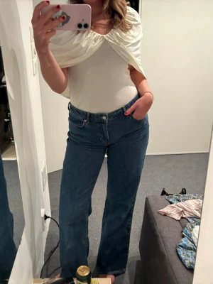 Vit omlott topp med twistad detalj - Säljer en vit omlott topp med snygg twistad detalj framtill. Toppen är ärmlös och har en elegant, draperad look. Materialet ser ut att vara mjukt och stretchigt, troligen bomull eller polyester. Perfekt för dig som gillar stilrena och trendiga plagg.