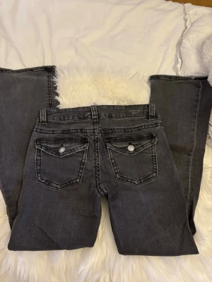 Svarta bootcut jeans från Perfect Jeans - Säljer ett par svarta bootcut jeans från Perfect Jeans. Jeansen har snygga bakfickor med lock och silverfärgade knappar. Modellen är utsvängd nertill och har en klassisk femficksdesign. Perfekta till en trendig vardagslook.