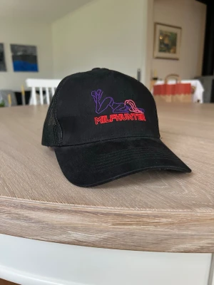 Svart truckerkeps MILFHUNTER - Säljer en svart truckerkeps med broderad MILFHUNTER-text och motiv i lila och rött framtill. Från Giga wear-> revenite som nu driver OneBoldChemist