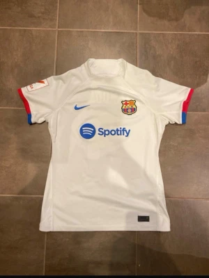 Vit FC Barcelona matchtröja Lewandowski 2023/2024 borta - Snygg vit FC Barcelona matchtröja från Nike med Lewandowski och nummer 9 på ryggen. Tröjan har klubbmärke, blå Nike-logga och Spotify som sponsor framtill. Röd och blå detalj. Den är äkta köpte den för 95€ i Barcelona säljer den för den ej passar. Sjukt snygg tröja lite använd eftersom den är inte använd på tränigar osv. Hör av er vid frågor!