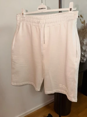 Vita shorts från Boss med snörning - Säljer ett par vita shorts från Boss med elastisk midja och snörning. Shortsen har två sidofickor, en bakficka och diskret Boss-logga broderad framtill. Tillverkade i mjuk bomull, perfekta för en avslappnad stil.