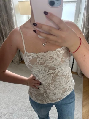 Vit spetslinnetopp med blommönster - Säljer en superfin vit spetslinnetopp med blommigt mönster och tunna axelband. . Perfekt att styla med jeans eller kjol för en trendig look.