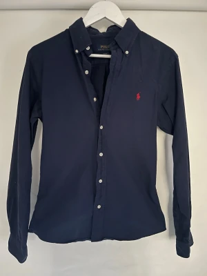 Mörkblå skjorta från Polo Ralph Lauren - Mörkblå skjorta från Ralph lauren i storlek S. Modell på bilden är 179 cm och väger 65kg. Finns tecken på användning men inga synliga defekter och skicket är bra. Tveka inte på att höra av dig vid frågor. Priset kan diskuteras.