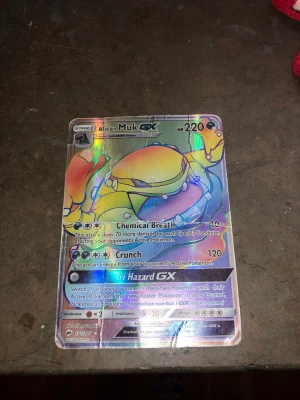 Pokémonkort Alolan Muk GX - Säljer ett holografiskt Pokémonkort, Alolan Muk GX med 220 HP. Kortet har färgstark design med metallic-effekt och visar Alolan Muk i gult och lila. Kortet har attacker som Chemical Breath, Crunch och Tri Hazard GX. Perfekt för samlare eller Pokémonfans. Kortet är också fejk