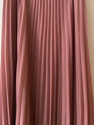 Atmosphere Plisserad rosa långkjol - Säljer en superfin plisserad långkjol i en mjuk rosa ton. Kjolen har ett luftigt fall och är perfekt för dig som gillar en flowy och elegant stil. Materialet känns lätt och skönt mot huden. Passar M, S