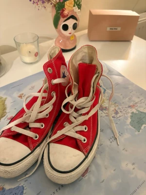 Röda Converse All Star high top - Klassiska röda Converse All Star high top sneakers med vit gummisula och tå, vita skosnören och metallöljetter. Ikonisk logga på sidan och svart rand längs sulan. Tillverkade i canvas som ger en cool och avslappnad vibe.