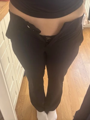 Svarta kostymbyxor med rak passform typ bootcut - Säljer ett par klassiska svarta kostymbyxor med rak passform och låg midja. Byxorna har diskreta fickor och stängs med knapp och dragkedja framtill. Perfekta till en stilren look och passar till många olika outfits.