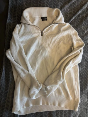 Vit ribbad tröja från Massimo Dutti - Snygg vit ribbad tröja från Massimo Dutti med halv dragkedja och hög krage. Tillverkad i mjukt material som ger en avslappnad men stilren look. Perfekt för lager på lager och enkel att matcha med jeans eller chinos.