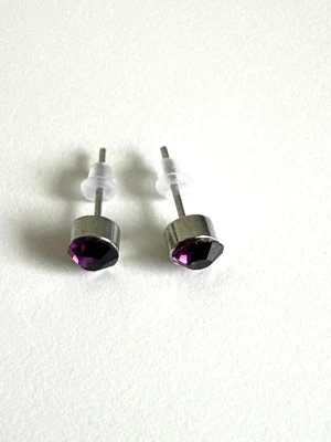 Silvriga örhängen med lila sten, helt NYA - Snygga örhängen i silverfärgad metall med rund, facetterad lila sten framtill. Stiften har transparenta pluppar för extra komfort. Perfekta för dig som gillar minimalistisk men ändå färgstark stil.
