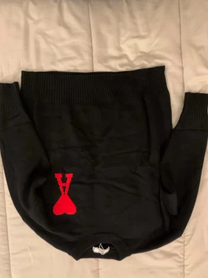 Svart stickad tröja från Ami Paris - Snygg svart stickad tröja från Ami Paris med deras ikoniska röda hjärta och A-logga broderad framtill. Tröjan har rund halsringning och ribbade muddar vid ärmslut och nederkant. Perfekt för dig som gillar stilrena plagg med en twist.