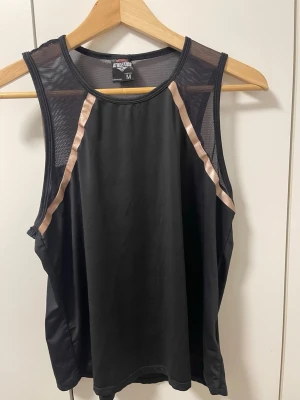 Svart träningslinne från Athletes - Snyggt svart träningslinne från Athletes med meshdetaljer upptill och texten 'READY TO MOVE' i rosa på ryggen. Linnet har ljusrosa ränder längs axlarna och är tillverkat i ett lätt och snabbtorkande material, perfekt för gym eller löpning.