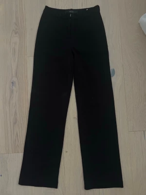 Svarta kostymbyxor från Vero Moda - Stilrena svarta kostymbyxor från Vero Moda med raka ben och klassisk passform. Byxorna har hällor för skärp, diskreta sidofickor och stängs med dragkedja och hake. Perfekta för en clean och snygg look.