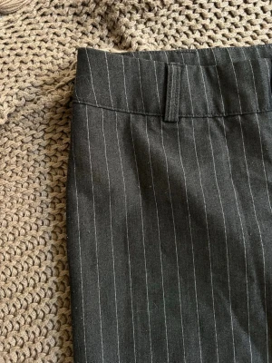 Randiga kostymbyxor från Madlady - Snygga kostymbyxor från Madlady i mörkgrått med tunna vita kritstrecksränder. Byxorna har klassisk passform med hällor för skärp och är perfekta för en stilren look. Materialet känns mjukt och följsamt.
