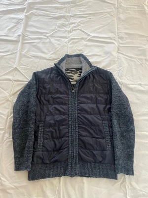 Grå stickad cardigan med quiltad front - Snygg cardiganjacka i mörkgrått med stickade ärmar och rygg samt quiltad front i svart. Dragkedja framtill, hög krage och två fickor. Perfekt lager-på-lager-plagg för kyliga dagar. Materialmix av stickat tyg och vadderad polyester framtill.