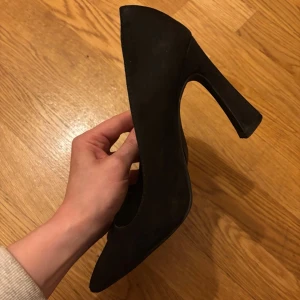 Svarta klackskor i mocka-look, wide fit - Säljer ett par svarta wide fit pumps med spetsig tå och hög men bred klack - som gör det väldigt enkelt att gå i! Skorna har en stilren design och är tillverkade i ett material som liknar mocka. Använda sparsamt. Storlek 38.