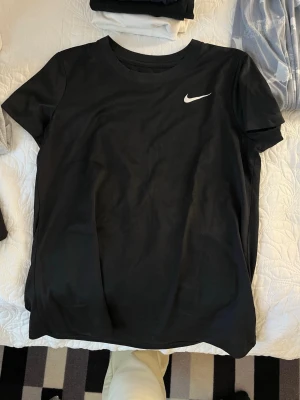 Svart Nike t-shirt med logga - Snygg svart t-shirt från Nike med klassisk vit logga på bröstet. T-shirten har rund halsringning och korta ärmar. Perfekt för en sportig och avslappnad stil.