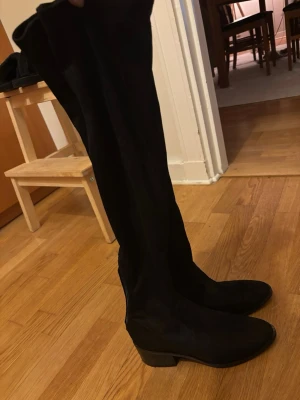 Steve Madden: Svarta overkneestövlar i mocka-look  - Säljer ett par svarta overknee stövlar med låg klack och rundad tå från Steve Madden. Stövlarna har en mjuk mocka-liknande yta och sitter tight längs benet och slutar precis ovanför knät. Vid knät sitter som en slags gummilist vilken säkerställer att stövlarna aldrig glider ner längst benet. Storlek 38, vanlig i storlek men aningen smala i sin form både vad de gäller foten och längs benet. 