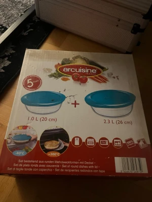 Arcuisine set med blå lock - Två runda glasburkar från Arcuisine med blå plastlock, en på 1,0 L (20 cm) och en på 2,3 L (26 cm). Perfekta för förvaring eller matlagning, tål både frys och ugn. Snygg design och praktiska att använda till olika ändamål. Aldrig använts och inte ens öppnad. 