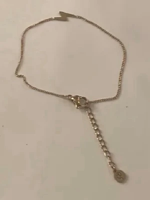 Guldigt armband med blixtberlock - Snyggt armband i guldfärgad metall med en cool blixtformad berlock framtill. Kedjan är tunn och har ett justerbart lås med en liten rund bricka i slutet. Perfekt för dig som gillar trendiga och unika smycken. Aldrig använd. Från Edblad!