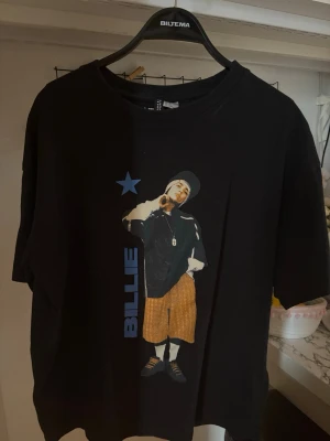 Billie Eilish svart t-shirt - Svart t-shirt med tryck av Billie Eilish på framsidan och turnélista på baksidan. T-shirten har korta ärmar, rund hals och tryck i blått, gult och vitt. Perfekt för dig som gillar streetwear och vill visa ditt stöd för Billie