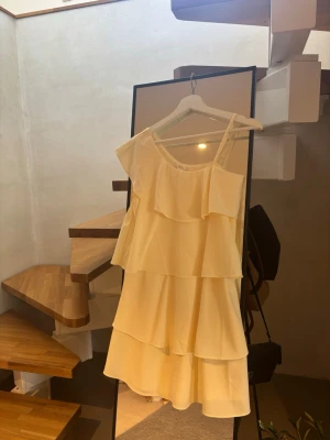 Ljusgul one shoulder klänning Gina Tricot - Supersöt ljusgul klänning från Gina Tricot med one shoulder-design och flera volanglager. Perfekt för sommarens alla tillfällen. Tillverkad i ett lätt och luftigt material.