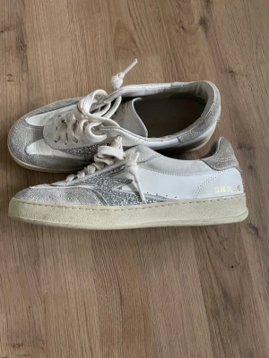 Vita och grå sneakers Moa Concept  - Snygga sneakers från Moa Concept i vitt och grått med glitterdetaljer på sidan. Skorna har en låg silhuett, vita skosnören och en beige sula. Materialmix av mocka och läder ger en trendig look. Perfekta för dig som gillar stilrena men ändå unika sneakers. Inköpta på NK, nypris 2600kr