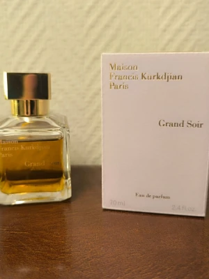 Maison Francis Kurkdjian Grand Soir - Exklusiv parfym från Maison Francis Kurkdjian, Grand Soir, i en elegant fyrkantig glasflaska med guldfärgat lock. Doften är en Eau de Parfum och flaskan rymmer 70 ml. Förpackningen är stilren och vit med guldfärgad text. Se bild för kvarvarande mängd.