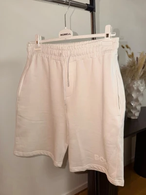 Vita sweatshorts från BOSS - Snygga vita sweatshorts från BOSS med broderad logga på benet. Shortsen har elastisk midja med snörning och sidofickor. Perfekta för en avslappnad och trendig look under varmare dagar.