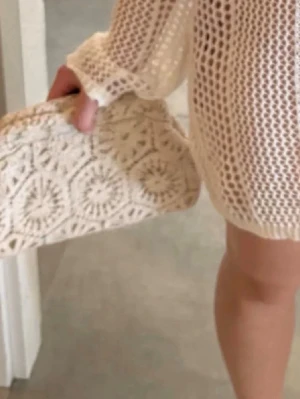 Beige virkad kuvertväska - Säljer en beige kuvertväska i virkad stil med snyggt mönster. Väskan har en mjuk, rektangulär form och är perfekt att bära i handen. Materialet är troligtvis bomull eller liknande textil och ger en bohemisk känsla. Skitsnygg clutch