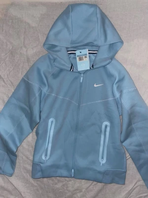 Blå set från Nike NOCTA - Säljer ett par ljusblå mjukisbyxor från Nike NOCTA-kollektionen. Byxorna har resår i midjan med dragsko, två fickor med dragkedja och NOCTA-logga på benet. Materialet är mjukt och stretchigt, perfekt för chill dagar. Swoosh-logga på låret för extra stil.