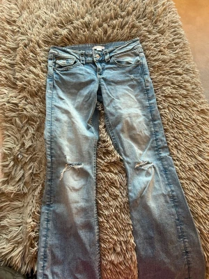 Blå bootcut jeans med slitningar - Säljer ett par ljusblå bootcut jeans med slitningar vid knäna och snygga detaljer på bakfickorna. Säljer pga att det är för små!