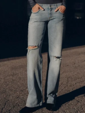 Zara jeans med slitningar - Säljer ett par ljusblå jeans med raka ben och slitna detaljer vid knäna. Jeansen har klassisk femficksmodell, hög midja och är tillverkade i denim. Perfekta för en avslappnad och trendig look. Liten i storlek!