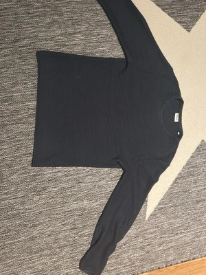 Mörkblå långärmad tröja - En stilren mörkblå långärmad tröja med rund halsringning. Tröjan har en enkel och klassisk design, perfekt att matcha med olika outfits. Materialet ser ut att vara mjukt och bekvämt, och passformen är rak.