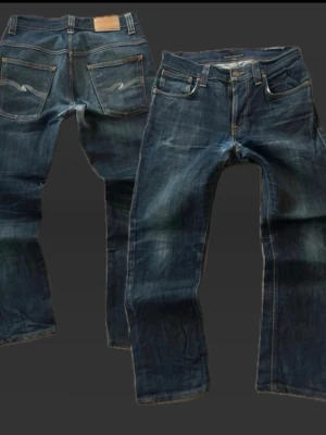  Nudie Jeans thin finn  - Säljer ett par mörkblå jeans från Nudie Jeans med klassisk femficksmodell och raka ben. Jeansen har snygga slitningar och kontrastsömmar samt Nudie Jeans ikoniska broderi på bakfickorna. Tillverkade i kraftig denim av bomull. Dom är professionellt upplagda dom är original 34 i längde men är nu 32/30! 