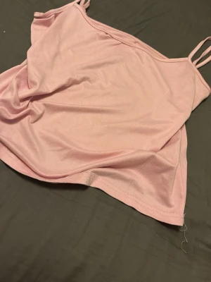 Ljusrosa linnetopp med smala band - Söt ljusrosa linnetopp med tunna axelband och enkel design. Toppen är ärmlös och har en mjuk, bekväm passform som passar perfekt till sommaren. Tillverkad i ett lätt material som känns skönt mot huden.