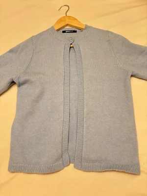 Ljusblå kofta från Gina Tricot - Söt ljusblå kofta från Gina Tricot med rund halsringning och knappstängning upptill. Koftan är ribbstickad vid ärmslut, nederkant och hals, och har en enkel, stilren design som passar perfekt till lager på lager.