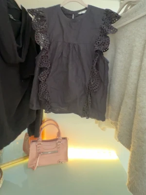 Svart blus med volangdetaljer från Cubus - Supersöt svart blus från C i storlek XS. Blusen har korta ärmar med breda volangdetaljer i broderad spets längs axlarna och sidorna. Rund halsringning och luftig passform, perfekt till både jeans och kjol. Materialet känns lätt och bekvämt.