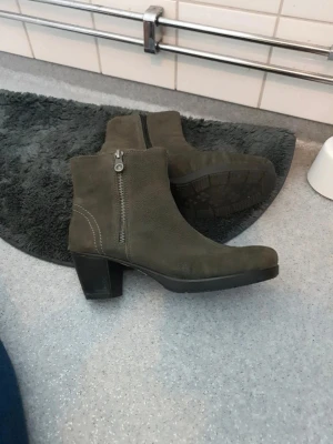 Mörkgröna mockastövletter med klack - Snygga mörkgröna stövletter i mocka med grov klack och dragkedja på sidan. Skorna har en stilren design med markerade sömmar och rundad tå. Perfekta för dig som vill ha en enkel men trendig look.