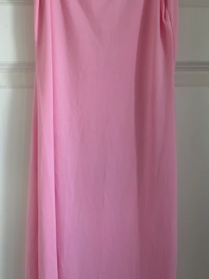 Lång rosa klänning  - En enkel och stilren långklänning i en mjuk rosa färg. Klänningen har en rak passform och är ärmlös, perfekt för varma dagar. Inga synliga detaljer eller mönster, vilket ger ett minimalistiskt och fräscht intryck.