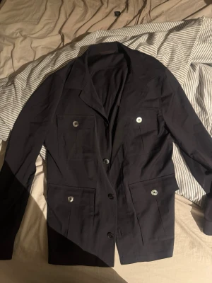 Marinblå overshirt från Oscar Jacobson - Stilren blå overshirt från Oscar Jacobson med fyra framfickor och knappar framtill. Klassisk krage och långärmad modell, perfekt för en dressad look. Materialet känns mjukt och följsamt.